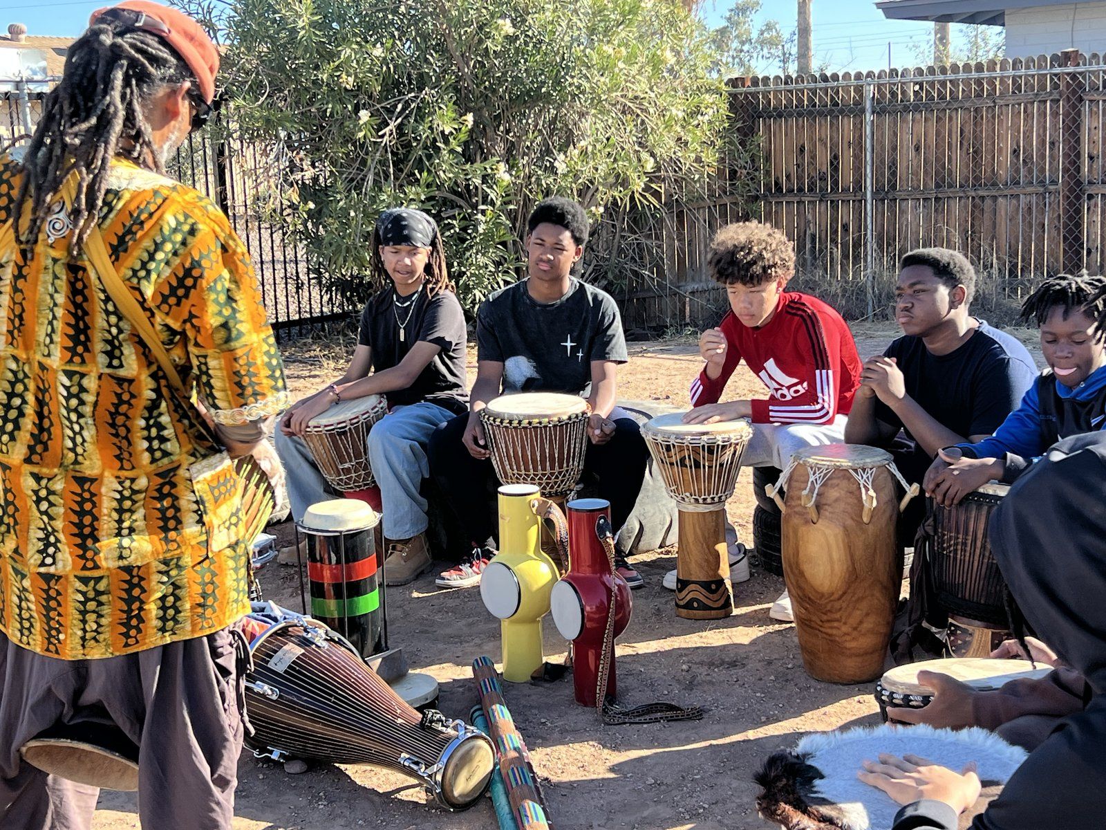 A drum instructor leading mentees seated with djembe drums outdoors