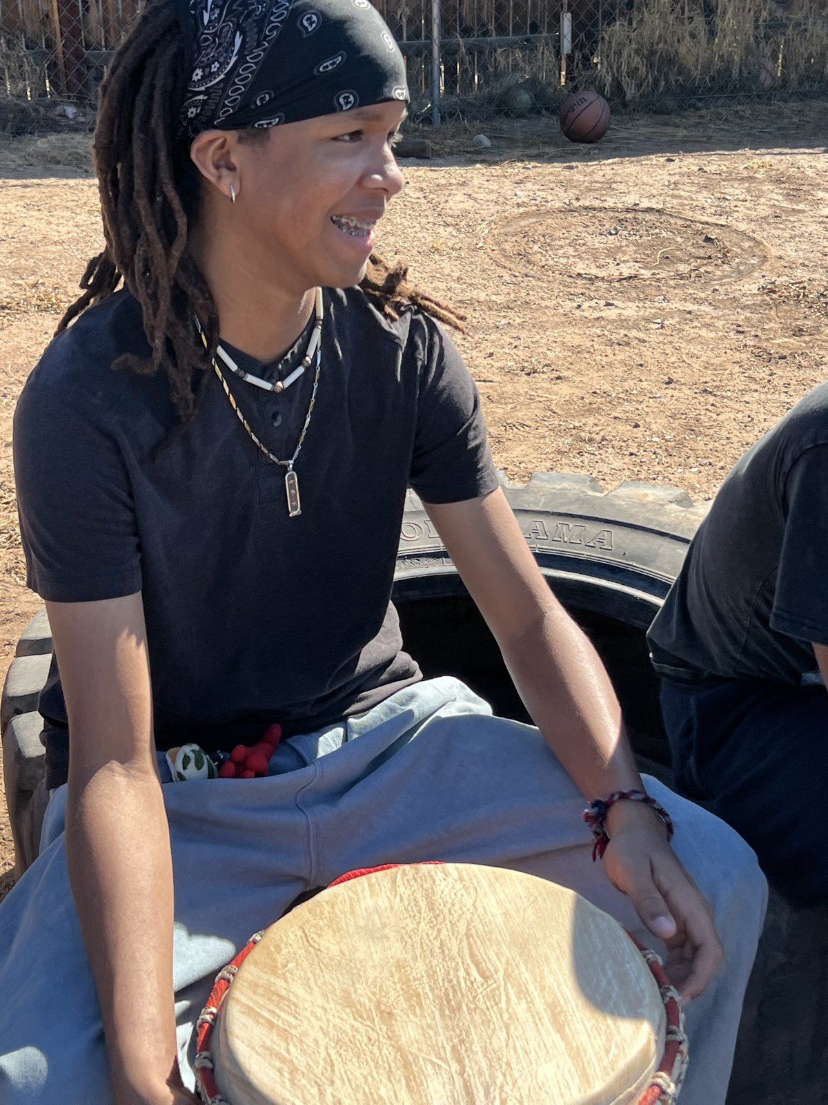 A mentee smiling behind a djembe drum during an outdoor drumming session