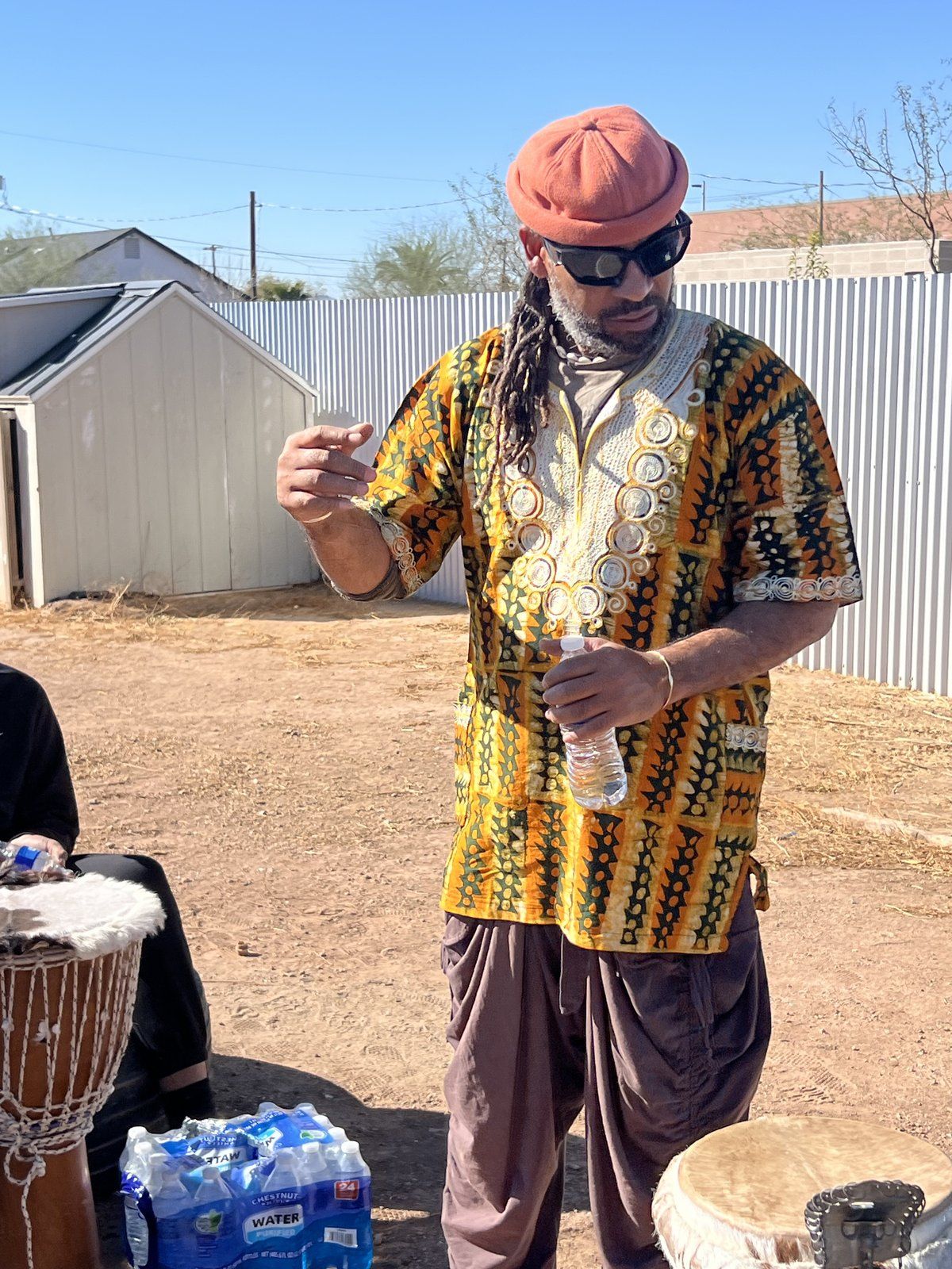 A drum instructor in traditional print addressing the group outdoors