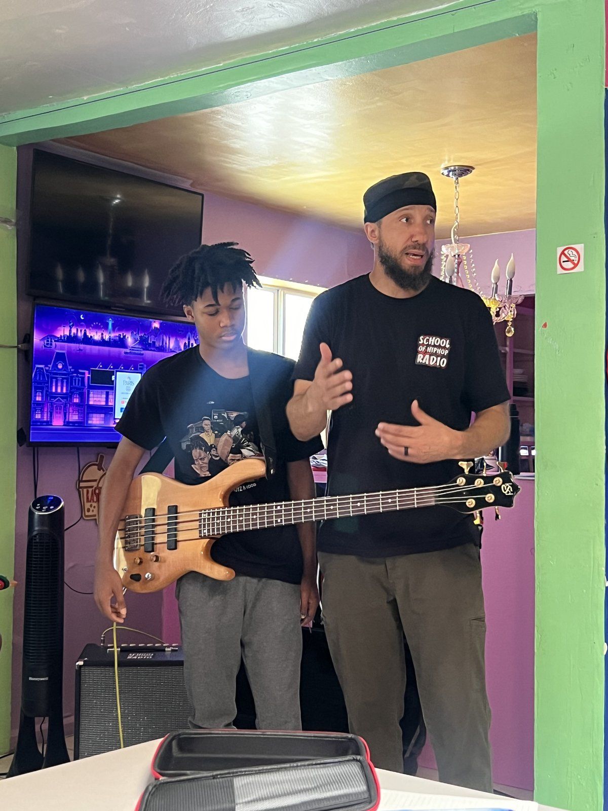 A music mentor with a bass guitar talking with a mentee in a studio space