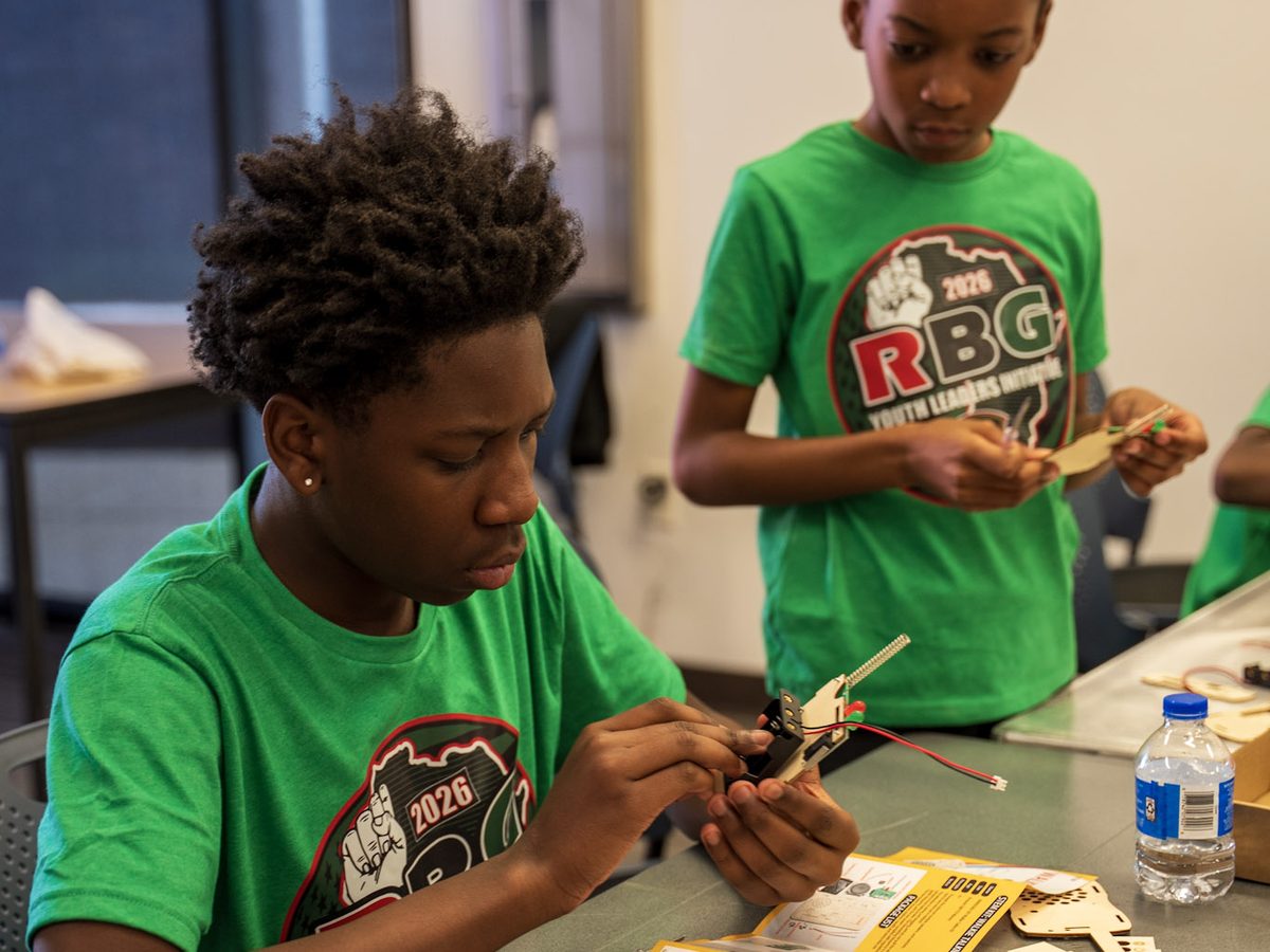 A young man in an RBG Youth Leaders shirt assembles a hands-on project at a workshop table.