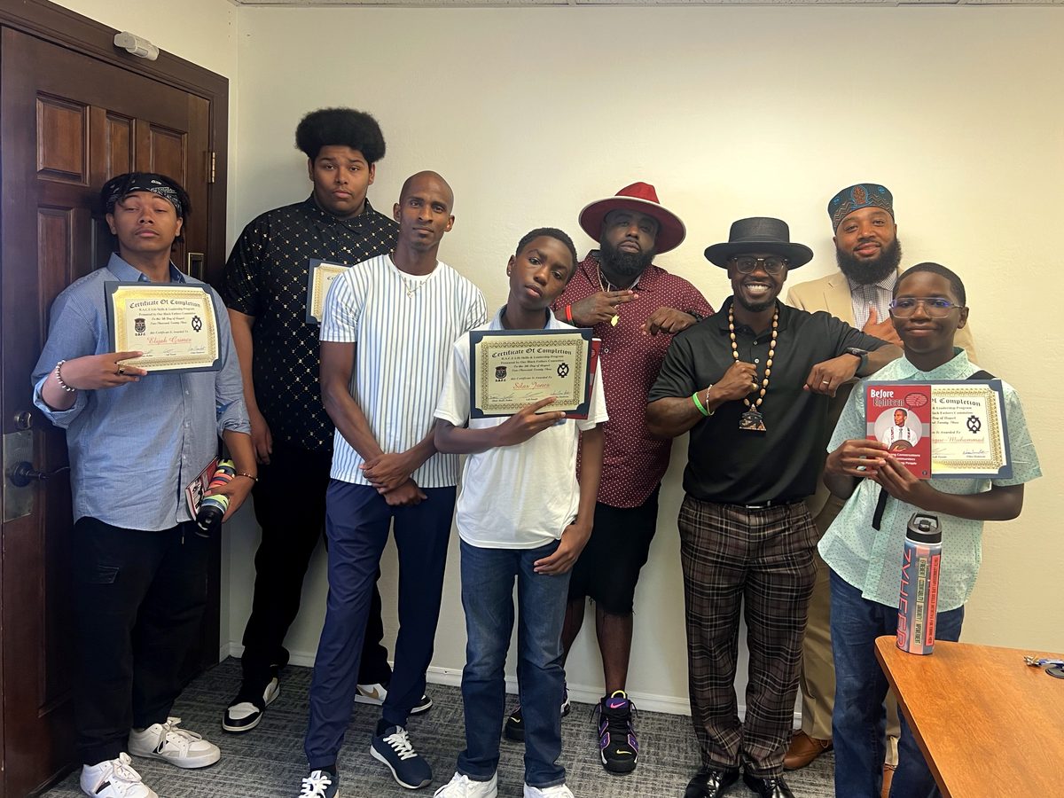 Young men hold their certificates alongside the mentors who saw them through the program.