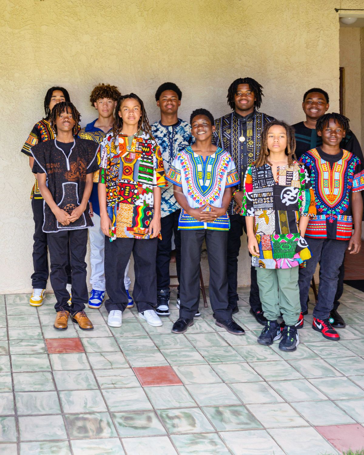 Ten OBFC Project mentees in dashikis and African print shirts standing together on a tiled patio